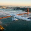 Avión de la aerolínea United Airlines sobrevolando el puente de San Francisco con vistas del mar y la ciudad al fondo cubiertas por un poco de nubes