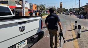 Miembro de la Policía de Investigación de la Fiscalía de Jalisco con un arma larga en la mano al lado de una camioneta blanca en una avenida de Tonalá