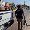 Miembro de la Policía de Investigación de la Fiscalía de Jalisco con un arma larga en la mano al lado de una camioneta blanca en una avenida de Tonalá