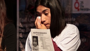 Mujer llora mietras sostiene un cartel de su hijo sustraído por su padre.