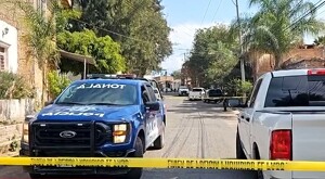Patrulla de la Policía Municipal de Tonalá estacionada al lado de una camioneta blanca y detrás de una cinta policiaca amarilla con casas y árboles alrededor