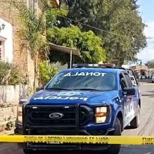 Patrulla de la Policía Municipal de Tonalá estacionada al lado de una camioneta blanca y detrás de una cinta policiaca amarilla con casas y árboles alrededor