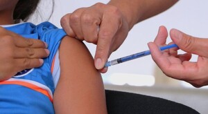 Niña con la manga de la playera levantada recibiendo la aplicación de una vacuna contra el sarampión