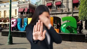 Mujer con el rostro tapado hace un ademán de 'alto' frente al edificio sede del Ayuntamiento de Puebla.