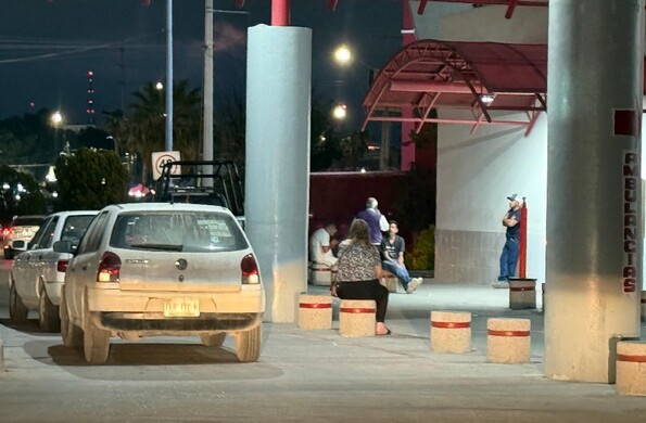 Se observa una camioneta blanca estacionada y al fondo unas personas sentadas.