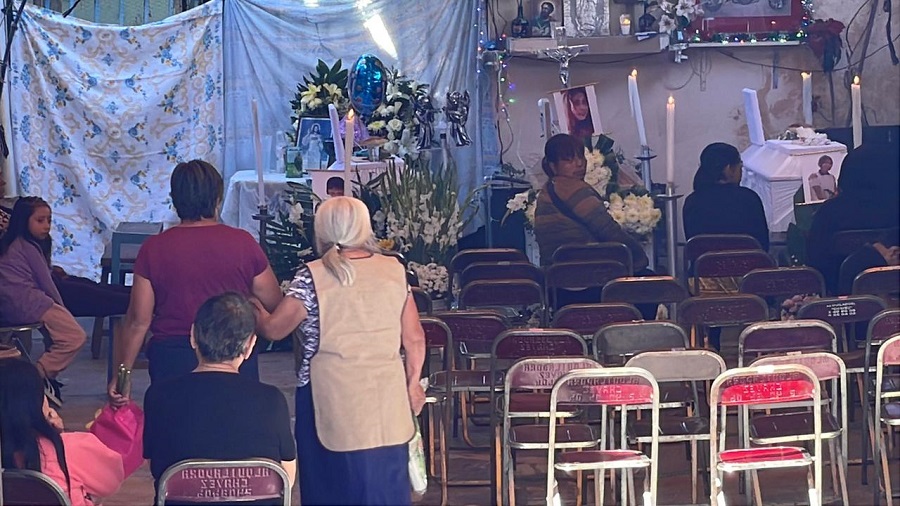 Personas asisten a un velorio donde hay fotos de dos mujeres sobre un féretro.
