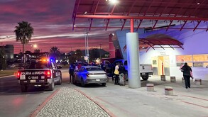 Se observa un edificio blanco con una cruz roja, es de noche, hay varios autos estacionados y genet afuera.