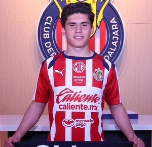 Jugador Jonathan Pérez vistiendo la jersey del equipo de las Chivas del Guadalajara parado delante del escudo del equipo