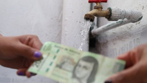 Personas intercambian un billete de 200 pesos mexicanos con una manguera de agua de fondo.