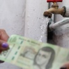Personas intercambian un billete de 200 pesos mexicanos con una manguera de agua de fondo.