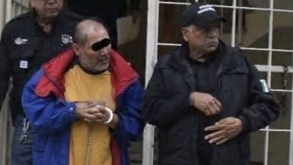 Hombre con esposas sobre las manos siendo conducido por policías.