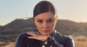 La cantante Yuridia viendo de frente a cámara con la mano apoyada sobre su mentón con un cerro desenfocado en el fondo durante la tarde