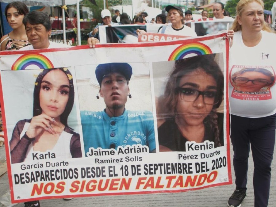 Dos mujeres sosteniendo un cartel con las fotos de tres personas desaparecidas durante una marcha con más manifestantes detrás