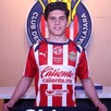 Jugador Jonathan Pérez vistiendo la jersey del equipo de las Chivas del Guadalajara parado delante del escudo del equipo