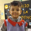 Niño Valentín Mercado Toledo sonriendo mientras ve a la cámara con un mandil de cuadros dentro de un salón de kínder con una niña a un lado y dibujos de fondo