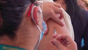 Se observa a una mujer aplicándole una inyección en el brazo de una persona.