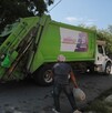 Se observa un camión de basura y dos hombres a lado de éste.