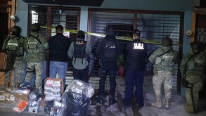 Se observa a varios hombres de espaldas, entre ellos a unos militares.