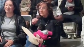 Regidora de Ocotlán, Silvia Iliana Villarruel Gutiérrez sentada y sosteniendo una cría de mono araña que viste un suéter rosa en medio de un evento público