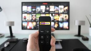 Logo de  Meli+ Mega sobre un control remoto y en el fondo una televisión con un menu desplegado sobre su pantalla