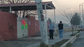 Se observa a dos mujeres paradas y enfrente de observan unas pancartas.
