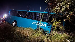 Camión de pasajeros color azul con la inscripción Aruza en un costado caída dentro de una zanja con árboles y maleza al lado de la carretera