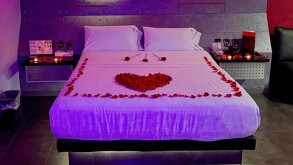 Cama de una habitación del Motel Kuboz en Zapopan con flores y pétalos de roza formando un corazón y con velas en los burós
