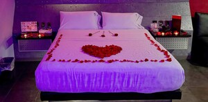 Cama de una habitación del Motel Kuboz en Zapopan con flores y pétalos de roza formando un corazón y con velas en los burós