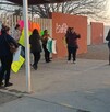 Se observa a varias personas paradas, afuera de una escuela, con pancartas en mano.