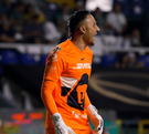 El portero Keylor Navas (Pumas) en un uniforme naranja brillante y guantes blancos grita de emoción en el campo. Está en un partido nocturno frente a las gradas