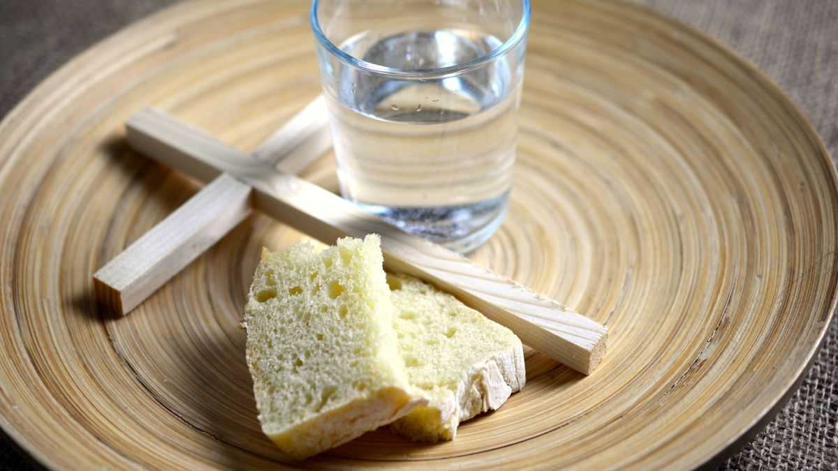 Un crucifijo sobre un plato con un vaso de vidrio con agua y dos piezas de pan