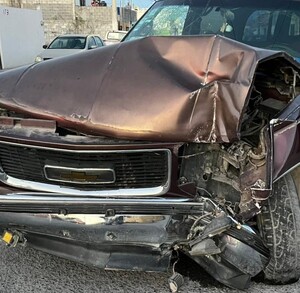 Se observa una camioneta negra con gris destrozada del frente y unos hombres parados al fondo.