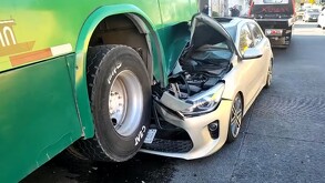 Vehículo tipo hatchback color gris con la parte frontal destruida y encajada debajo de la rueda de un camión verde de transporte público en Guadalajara