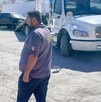 Hay una camioneta negra al fondo, una grúa y un hombre que viste playera gris y pantalón negro.