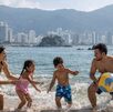 Familia disfrutando de las vacaciones de semana santa y jugando frente al mar de Acapulco con una pelota en un día soleado.