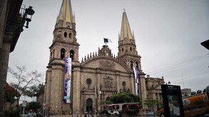 Vista de la fachada principal de la Catedral de Guadalajara con un cielo nublado y calandrias, un turibús y personas caminando alrededor