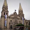 Vista de la fachada principal de la Catedral de Guadalajara con un cielo nublado y calandrias, un turibús y personas caminando alrededor