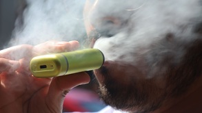 Persona sacando humo mientras utiliza un vapeador.