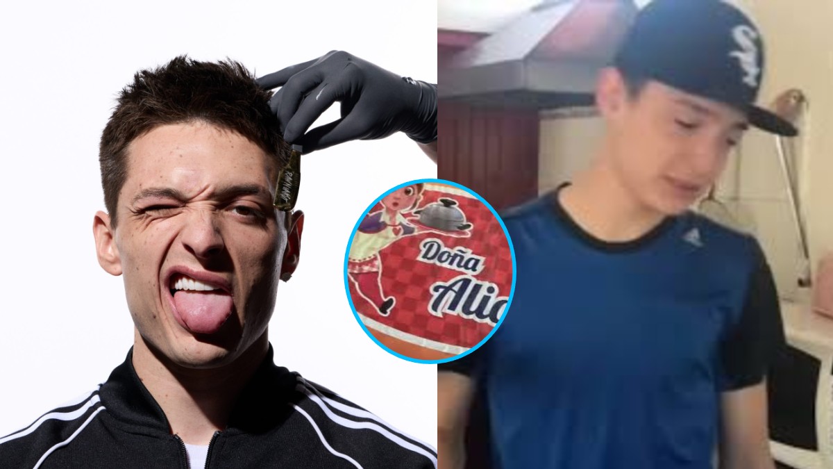 Peso Pluma con expresión burlona saca la lengua mientras una mano con guante negro sostiene una pequeña placa dorada cerca de su sien derecha.