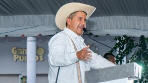 Carlos Manzo hablando por un micrófono delante de un podio durante una presentación pública en Uruapan