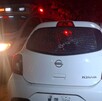 Vista de la parte trasera de un carro Nissan March color blanco con el cristal roto por impactos de bala y una ambulancia estacionada a un lado
