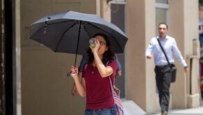 Mujer tomando agua con sombrilla y caminando.
