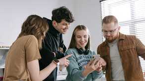 Un grupo de amigos viendo un celular mientras ríen por el contenido que ven el el dispositivo