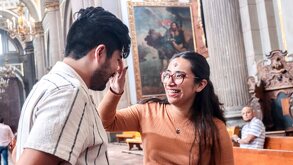 una mujer joven pinta una cruz de ceniza a un hombre joven dentro de una iglesia