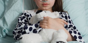 Niña hospitalizada sujetando un oso de peluche.