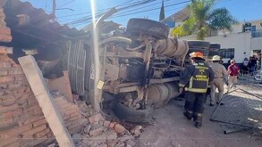 Camión de volteo volcado sobre la pared de una casa con oficiales de Protección Civil y Bomberos de Tlaquepaque a un lado