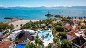 Vista aérea del Resort Kovay Gardens en Nayarit con estancias de lujo, palmeras, piscinas y una vista al mar con barcos y un faro