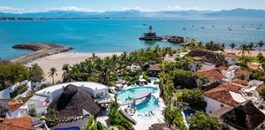 Vista aérea del Resort Kovay Gardens en Nayarit con estancias de lujo, palmeras, piscinas y una vista al mar con barcos y un faro
