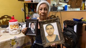 Se observa a una mujer de la tercera edad canosa, con dos cuadros con fotografías en las manos.