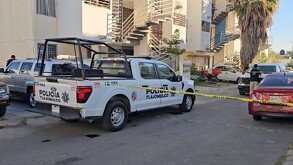 Patrulla de la Policía de Tlajomulco sosteniendo una cinta policiaca que acordona la calle afuera de edificios de departamentos con autos alrededor